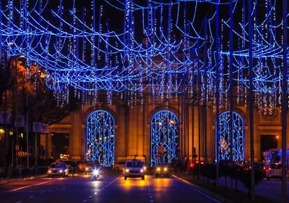 Los coches pasan por debajo de las luces de Navidad en la Puerta de Alcalá.