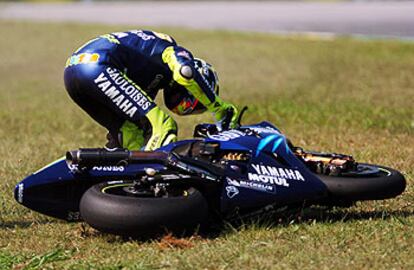 Rossi intenta levantar su moto del césped tras el accidente sufrido.