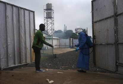 Un trabajador sanitario roc&iacute;a a un posible enfermo de &eacute;bola a la entrada de un centro de tratamiento de Monrovia (Liberia).