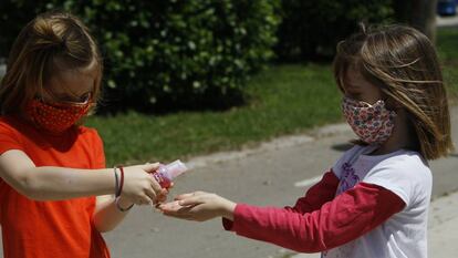 Dos niñas con mascarillas se limpian las manos con solución hidroalcohólica.