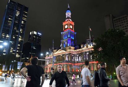 Els ciutadans caminen pels voltants de l'Ajuntament de Sydney, il·luminat amb els colors de la bandera de la república francesa en homenanje a les víctimes de l'atemptat. El primer ministre de l'Estat de Nova Gal·les, al sud d'Austràlia, ha demanat una bandera gegant de França per penjar-la del port de la Badia de Sydney.