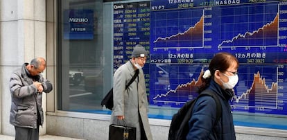 Viandantes en Tokio caminan frente a un video wall con índices bursátiles.