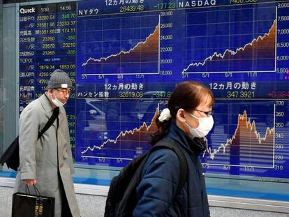 Viandantes en Tokio caminan frente a un video wall con índices bursátiles.