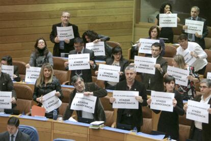 Diputados del PSdeG y el BNG levantan al unísono carteles de protesta durante el pleno del Parlamento autónomo.