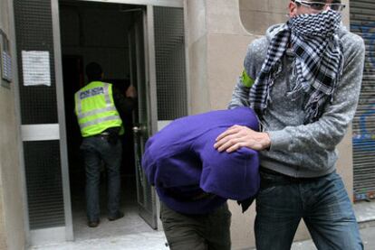 Un agente de los Mossos d'Esquadra traslada a un detenido en Poble Sec como presunto implicado en la red de pedofilia.
