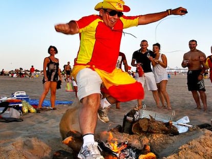 Un hombre ataviado con la bandera de Espa&ntilde;a salta una de las primeras hogueras encendidas en la playa en Valencia. 