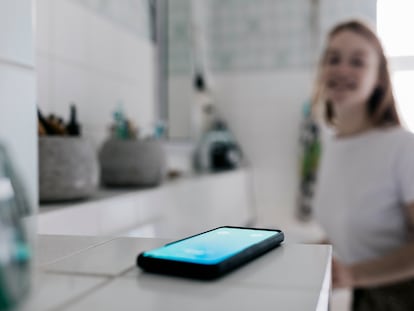 Un smartphone sonando en un cuarto de baño, mientras una mujer mira al fondo.