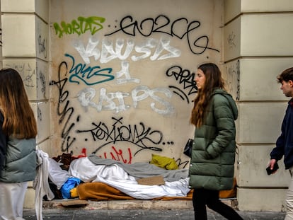 Varios jóvenes caminan frente a una persona que duerme en la calle en Madrid.