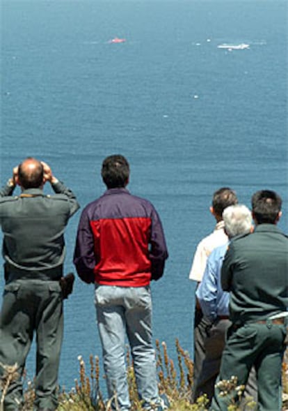 Dos guardias civiles y varios vecinos observan a las lanchas de Salvamento.