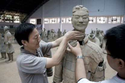 Dos arqueólogos trabajan en la restauración de la estatua de un guerrero.