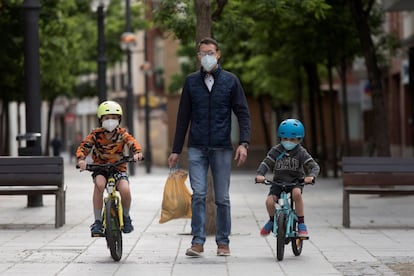 Unos niños en bicicleta pasean con su padre en Huesca con mascarillas para evitar contagios de covid-19.