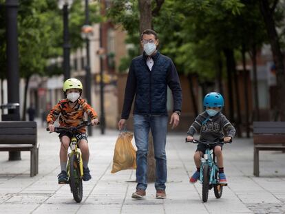 Unos niños en bicicleta pasean con su padre en Huesca con mascarillas para evitar contagios de covid-19.