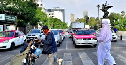 Un hombre camina con sus pertenencias frente a una mujer protegida con traje de bioseguridad el pasado martes en el Centro Histórico de la Ciudad de México (México).