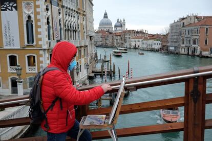 Un hombre protegido con una mascarilla pinta un cuadro sobre el puente de la Academia de Venecia.