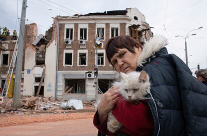 Una mujer sujeta a su gato junto a varios edificios destruidos en Járkov, este viernes. 