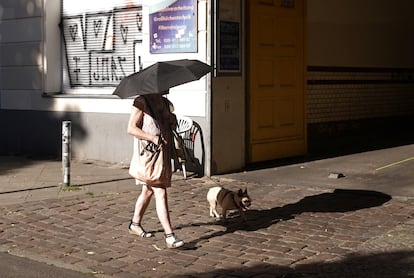 Una mujer pasea a su mascota protegida del calor por un paraguas en Berlín, este martes. 