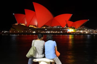 Turistas chinos contemplan el edificio de la Ópera de Sidney (Australia) iluminada de rojo para celebrar el Año Nuevo Chino.