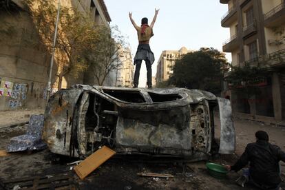 Un manifestante, de pie sobre un coche quemado, desafía a la policía durante las protestas en El Cairo