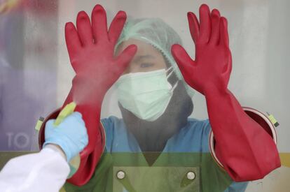 Una sanitaria rocía los guantes de goma de su compañera con desinfectante en una zona de pruebas de covid del laboratorio Genomik, en Yakarta, (Indonesia).