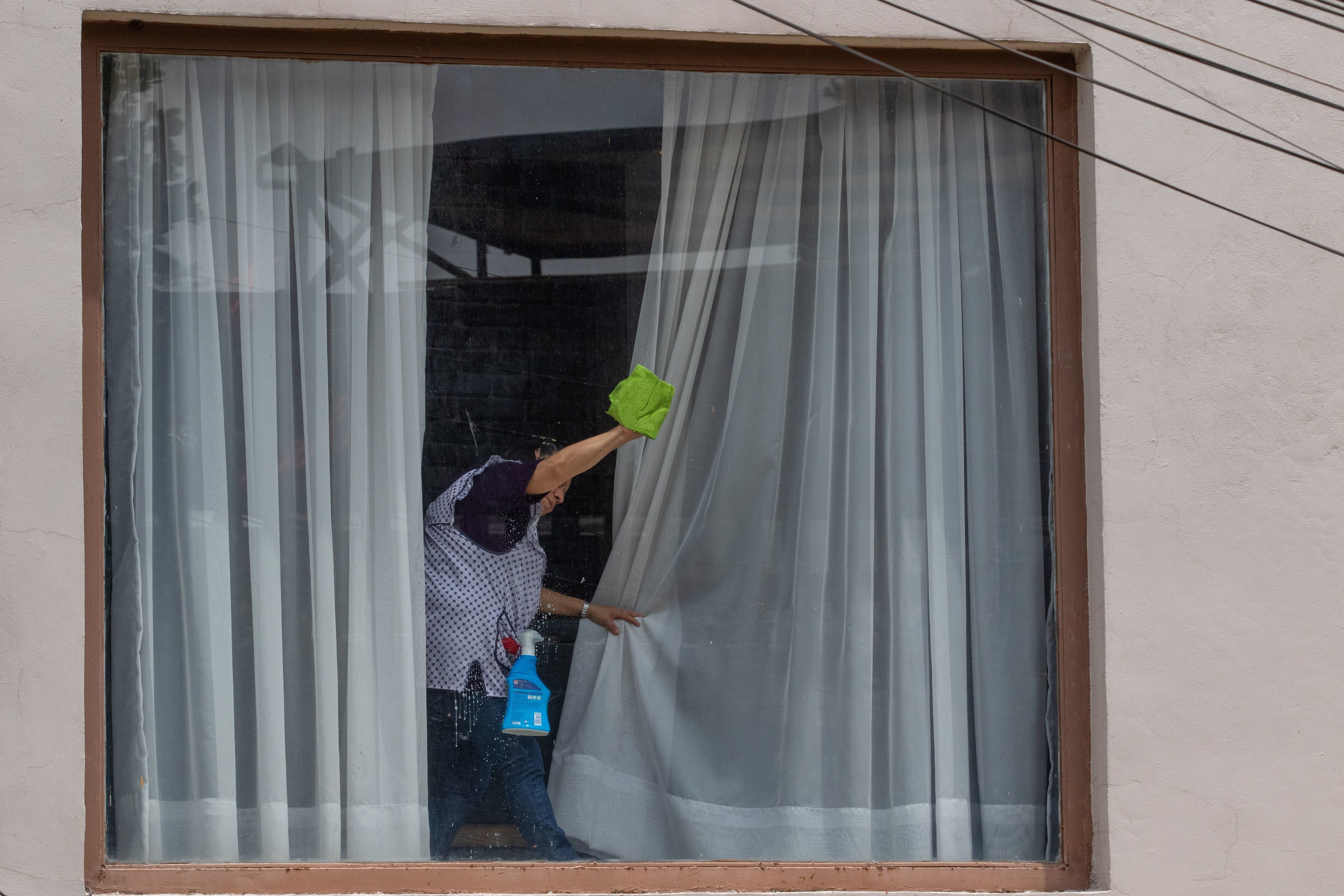 Una trabajadora del hogar limpia una ventana en una casa en la colonia Lomas de Virreyes, en Ciudad de México, en agosto de 2022.  