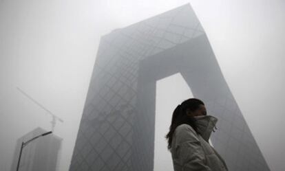 Una mujer camina junto a la sede de la televisión pública china en Pekín en medio de una intensa niebla mezcla de bruma y polución