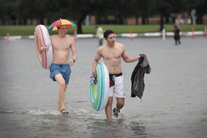 Dois jovens com boias caminham pelo campus de uma universidade alagado.