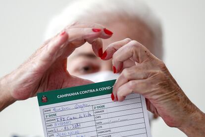 Uma idosa faz o formato de um coração com as mãos ao mostrar o atestado de vacinação contra covid-19 em São Paulo.