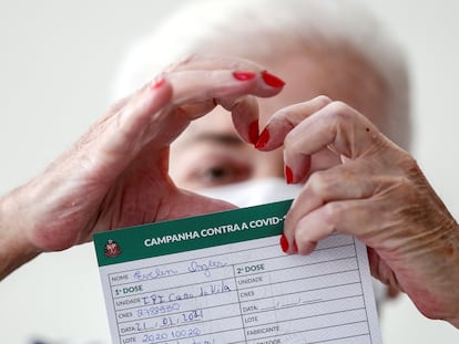 Uma idosa faz o formato de um coração com as mãos ao mostrar o atestado de vacinação contra covid-19 em São Paulo.