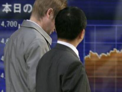 Dos peatones pasan por delante de una pantalla electrónica con el cierre de la Bolsa de Tokio (Japón). EFE/Archivo
