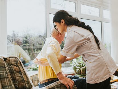 Una cuidadora ayuda a levantarse a una persona dependiente.