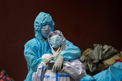 Dos mujeres indias con protección velan el cuerpo de un familiar fallecido por la covid, en un crematorio de Gauhati (India).)