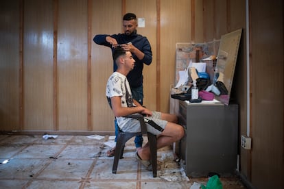 Un inmigrante peluquero corta el pelo a un compatriota en una de las naves abandonadas en la que viven.