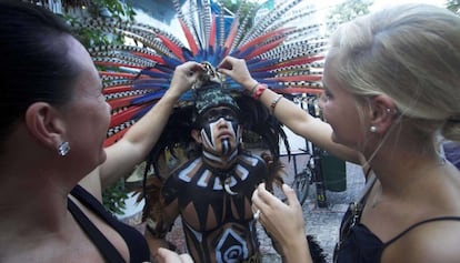 Dos turistas alemanas meten dinero en el casco de un actor-maya.