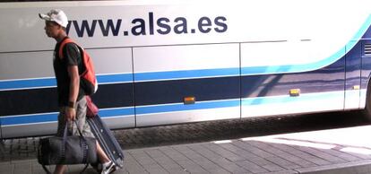 Un joven marcha con equipaje junto a un autobús de Alsa.