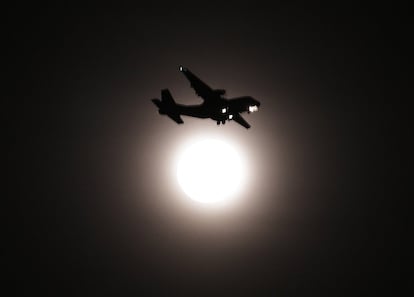 Un avión pasa por delante de la luna llena. 