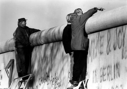 Quatro pessoas sobem em escadas e olham por cima do Muro de Berlim para o outro lado da cidade.