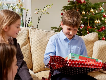 Un niños de 11 años abriendo un regalo en el sofá de sus casa.