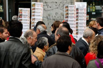 Varias personas pasan junto a un puesto de lotería en la Puerta del Sol en Madrid.