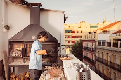 Pablo saca un queso fundido de su tradicional parrilla argentina, que ha instalado en el balcón de su apartamento en el centro de Madrid. La leña se carga en el brasero, y una vez que las ascuas caen al fondo, se colocan debajo de la parrilla principal.