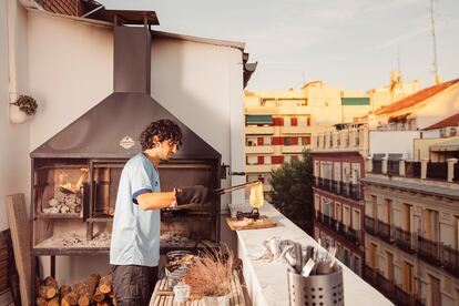 Pablo saca un queso fundido de su tradicional parrilla argentina, que ha instalado en el balcón de su apartamento en el centro de Madrid. La leña se carga en el brasero, y una vez que las ascuas caen al fondo, se colocan debajo de la parrilla principal.