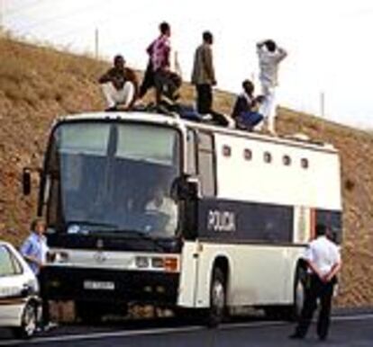 Los agentes vigilan a siete a siete inmigrantes amotinados tras la huida de dos más. Abajo, uno de ellos tras ser bajado del techo del autobús.