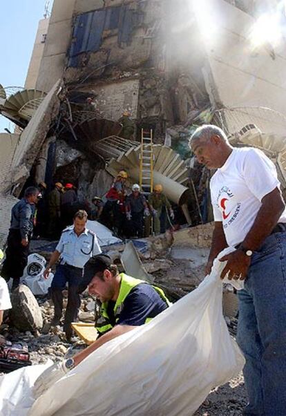 Un voluntario egipcio (a la derecha) y un israelí cubren un cadáver frente a los restos del hotel Hilton de Taba.