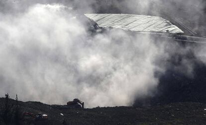 Una máquina trabaja en la zona del desprendimiento bajo el humo de los incendios.