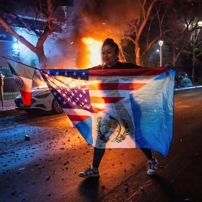 A person displaying multiple flags walks past a burning car during protests over the Trump administration's immigration raids in Los Angeles, Monday, June 9, 2025. (AP Photo/Ethan Swope)