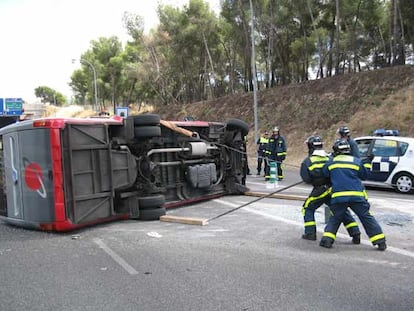 Los bomberos intentan levantar un minibús que volcó ayer en Madrid. Cuatro personas resultaron heridas.