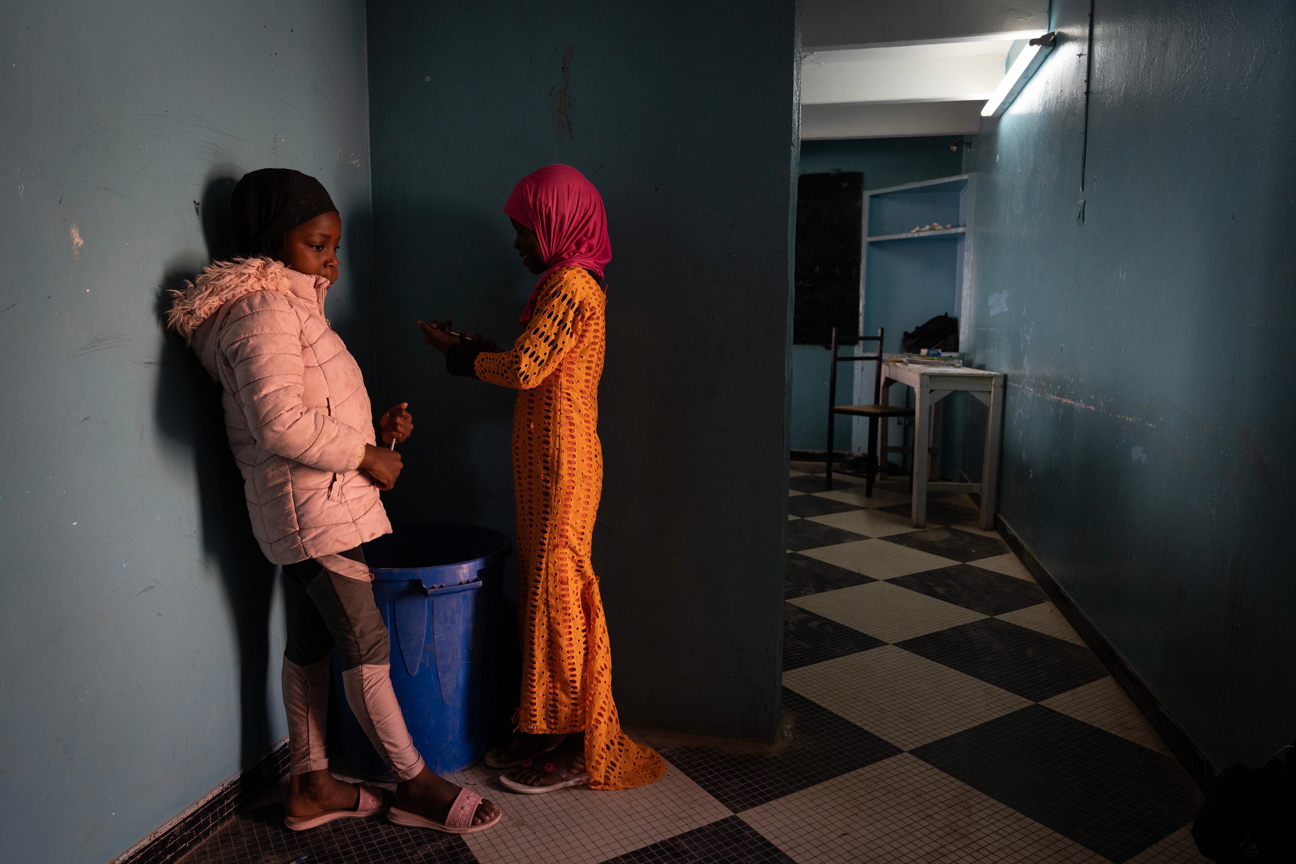 Dos niñas afilan sus lápices en un pasillo de la escuela.