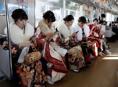 Jóvenes japonesas ataviadas con kimonos consultan sus móviles mientras regresan en tren tras participar en una fiesta en el parque de atracciones de Toshimaen, de Tokio con motivo de su mayoría de edad, en Japón.