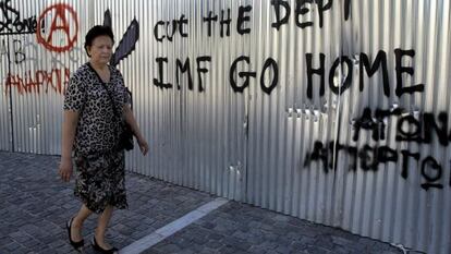 Una dona camina davant un grafiti en què es pot llegir "FMI vés-te'n a casa, talla el deute", a Atenes.