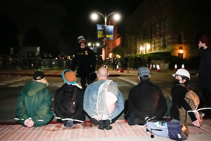 Cinco manifestantes esperan sentados tras ser detenidos por la policía durante el desalojo en la universidad este jueves.