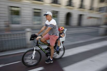 Un señor mayor circula con un niño pequeño en el transportín por el carril bici de la calle de Alcalá de Madrid.